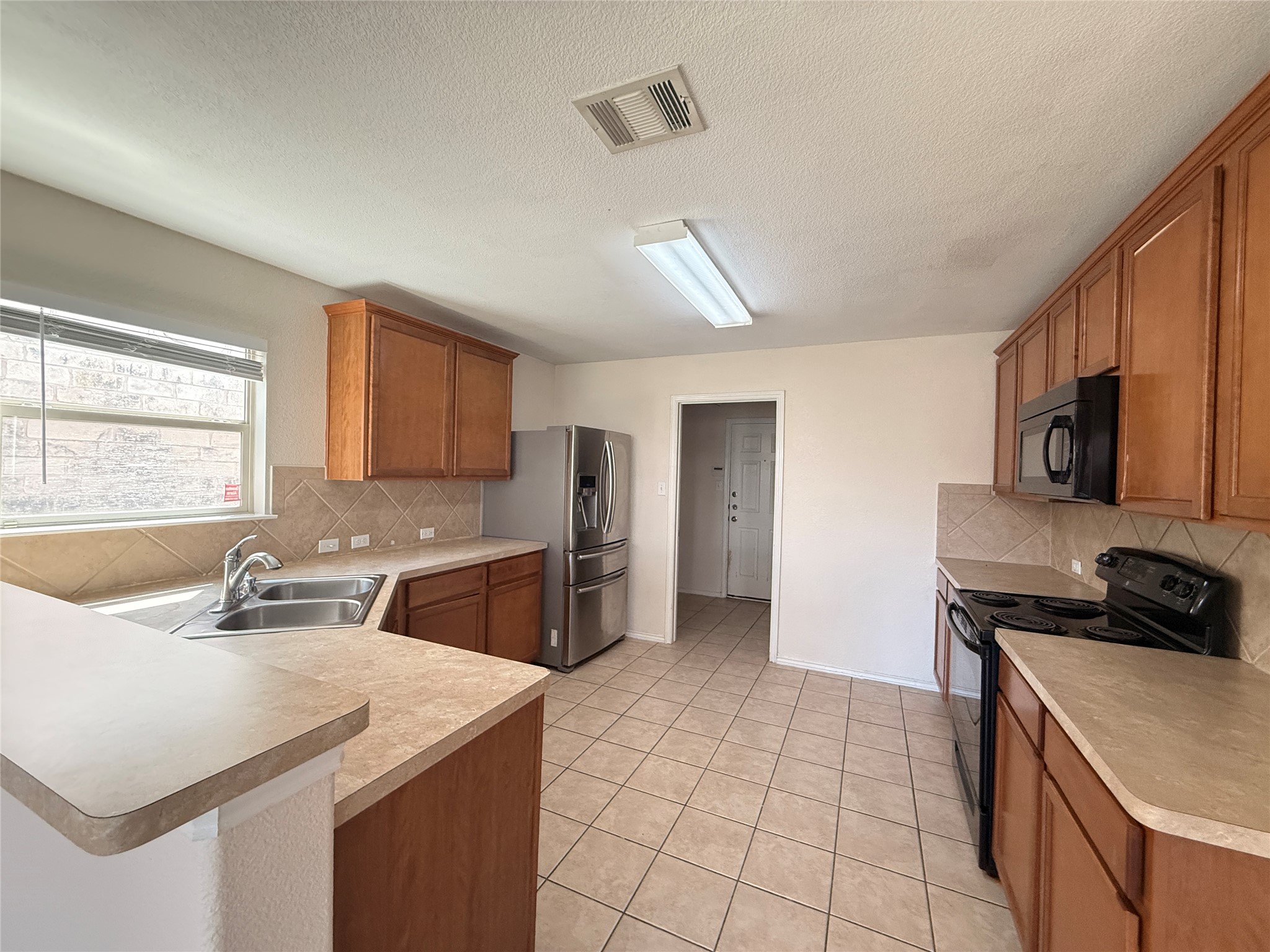 279 Housefinch Loop Leander, TX 78641 - Photo 8 of 30 Kitchen featuring wood finish cabinetry, black appliances, light countertops, a peninsula, and a textured ceiling