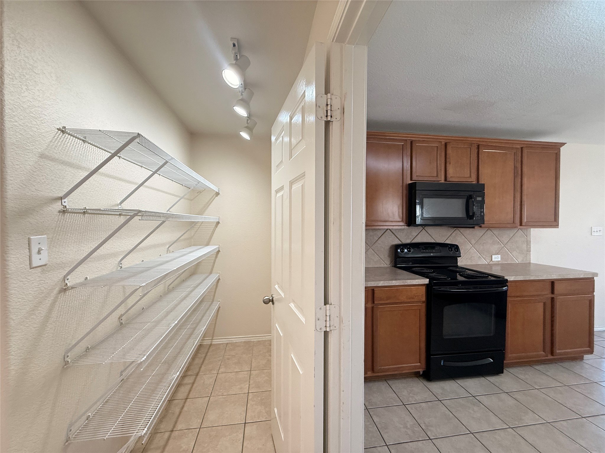 279 Housefinch Loop Leander, TX 78641 - Photo 9 of 30 Kitchen with wood finish cabinetry, black appliances, light countertops, light tile patterned floors, and tasteful backsplash