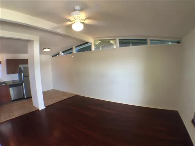 an empty room with wooden floor and way to kitchen
