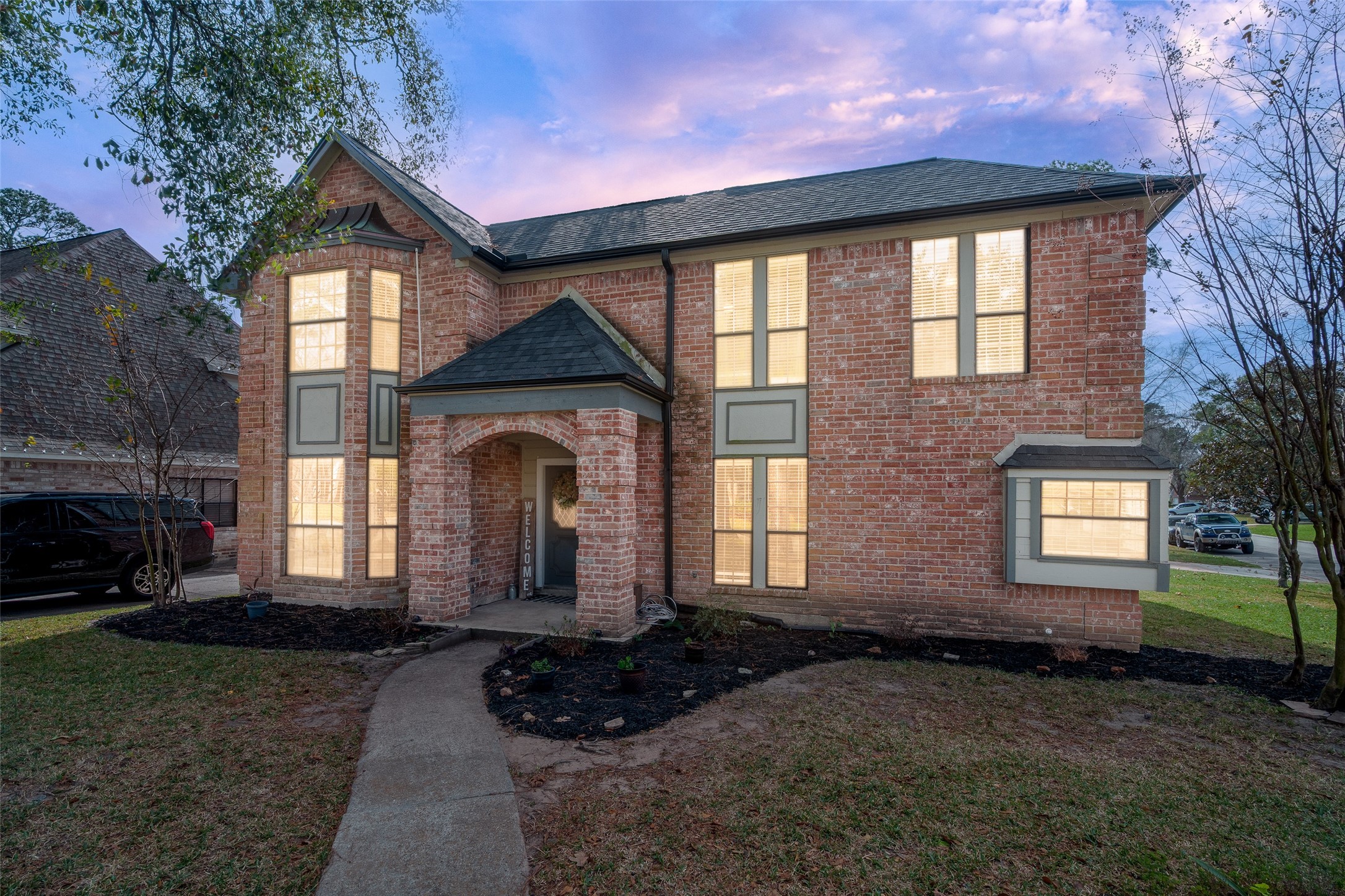 41 Windsor Drive Conroe, TX 77304 - Photo 39 of 39 Evening exterior view showcasing the home’s brick façade and welcoming front entry, with warm interior lighting creating a cozy nighttime ambiance. The arched covered entry and mature surroundings highlight the home’s curb appeal in the Rivershire community. Schedule a private showing to experience this home in person!