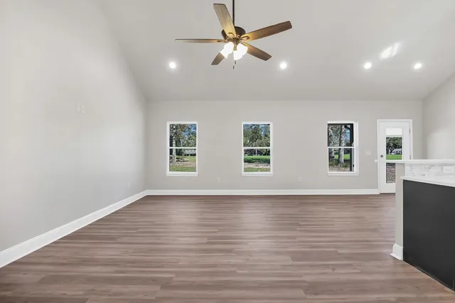 an empty room with wooden floor ceiling fan and windows