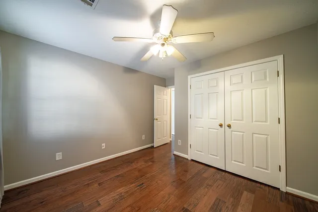 an empty room with wooden floor fan and windows