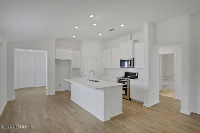 a kitchen with stainless steel appliances a stove top oven a sink a refrigerator and white cabinets