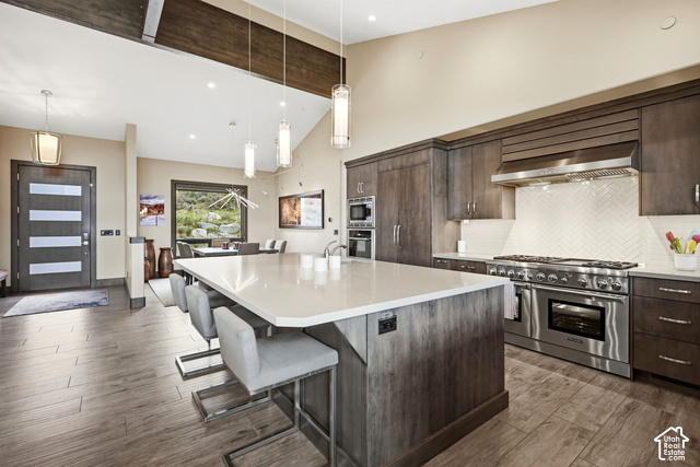 1130 Pace Road Park City, UT 84098 - Photo 24 of 73 Open-concept kitchen featuring an expansive island with seating, integrated stainless steel appliances, a herringbone tile backsplash, and wood-finish flooring