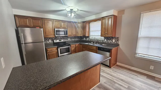 a kitchen with stainless steel appliances granite countertop a refrigerator a stove a sink dishwasher and white cabinets with wooden floor