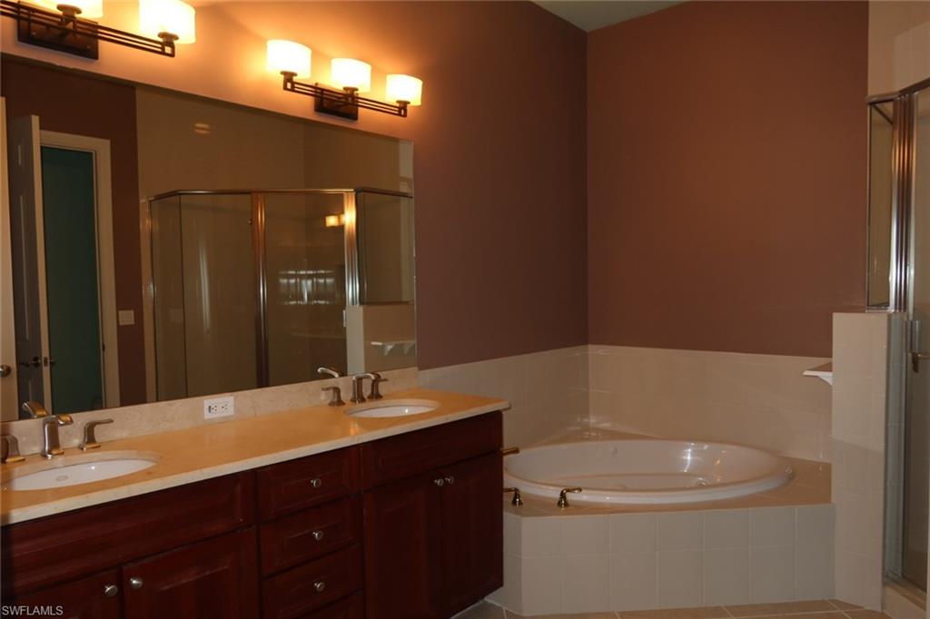 7168 Lemuria Circle, Unit 1701 Naples, FL 34109 - Photo 22 of 39 Double vanity with dual sinks, a large framed mirror, and a built-in jetted tub