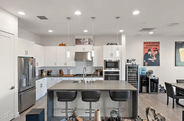 a kitchen with stainless steel appliances granite countertop a refrigerator a stove a sink a dining table and chairs with wooden floor