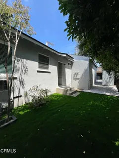 a backyard of a white house with potted plants and large tree