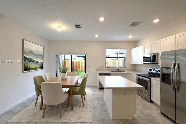 a kitchen with stainless steel appliances kitchen island granite countertop a dining table chairs and refrigerator