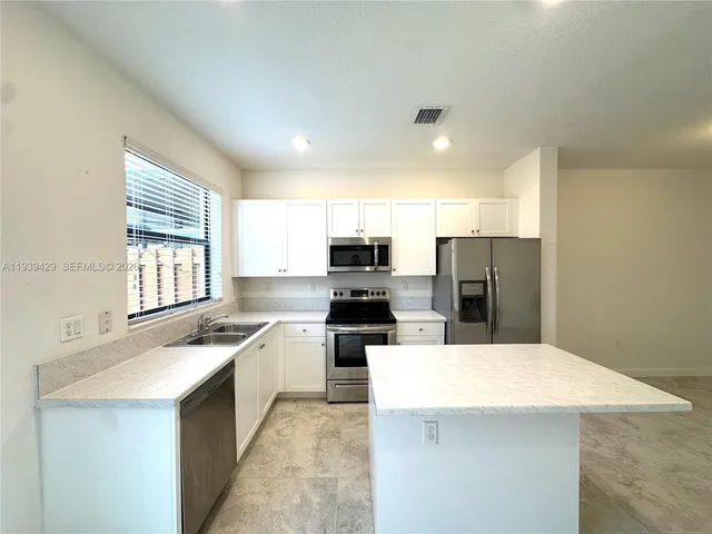 a kitchen with stainless steel appliances a refrigerator a stove a sink and white cabinets