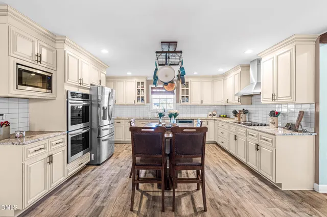 a kitchen with stainless steel appliances granite countertop a stove top oven a sink dishwasher a dining table and chairs with wooden floor