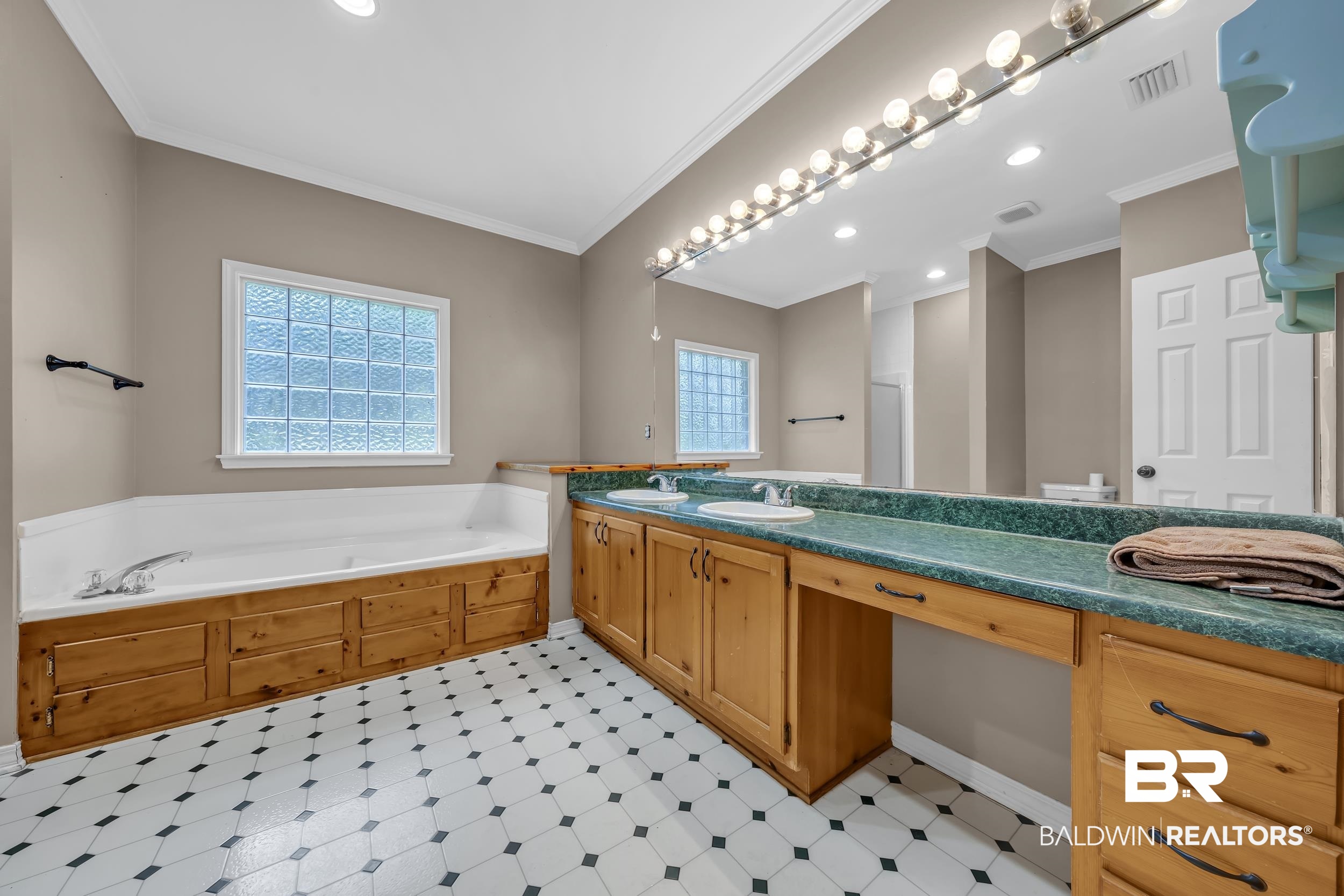 14960 Howells Ferry Road Wilmer, AL 36587 - Photo 13 of 22 Full bath featuring a built-in soaking tub with wood-finish paneling, a dual vanity with a green countertop, and a large wall mirror with vanity lighting