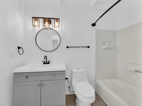 a bathroom with a toilet sink vanity granite tub and mirror