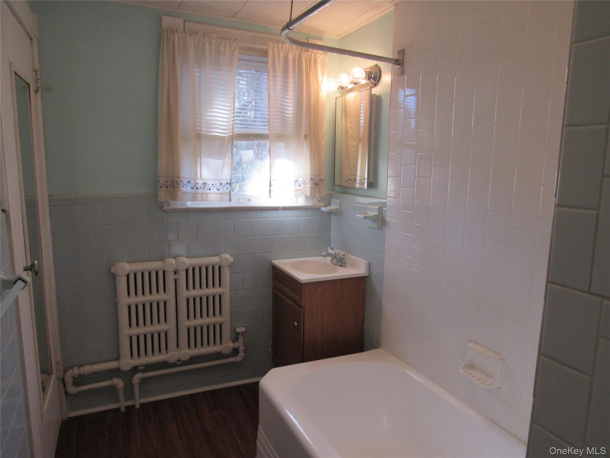 98 Main Street Chester, NY 10918 - Photo 26 of 32 Full bath featuring tile walls, radiator heating unit, vanity, dark wood-style floors, and wainscoting