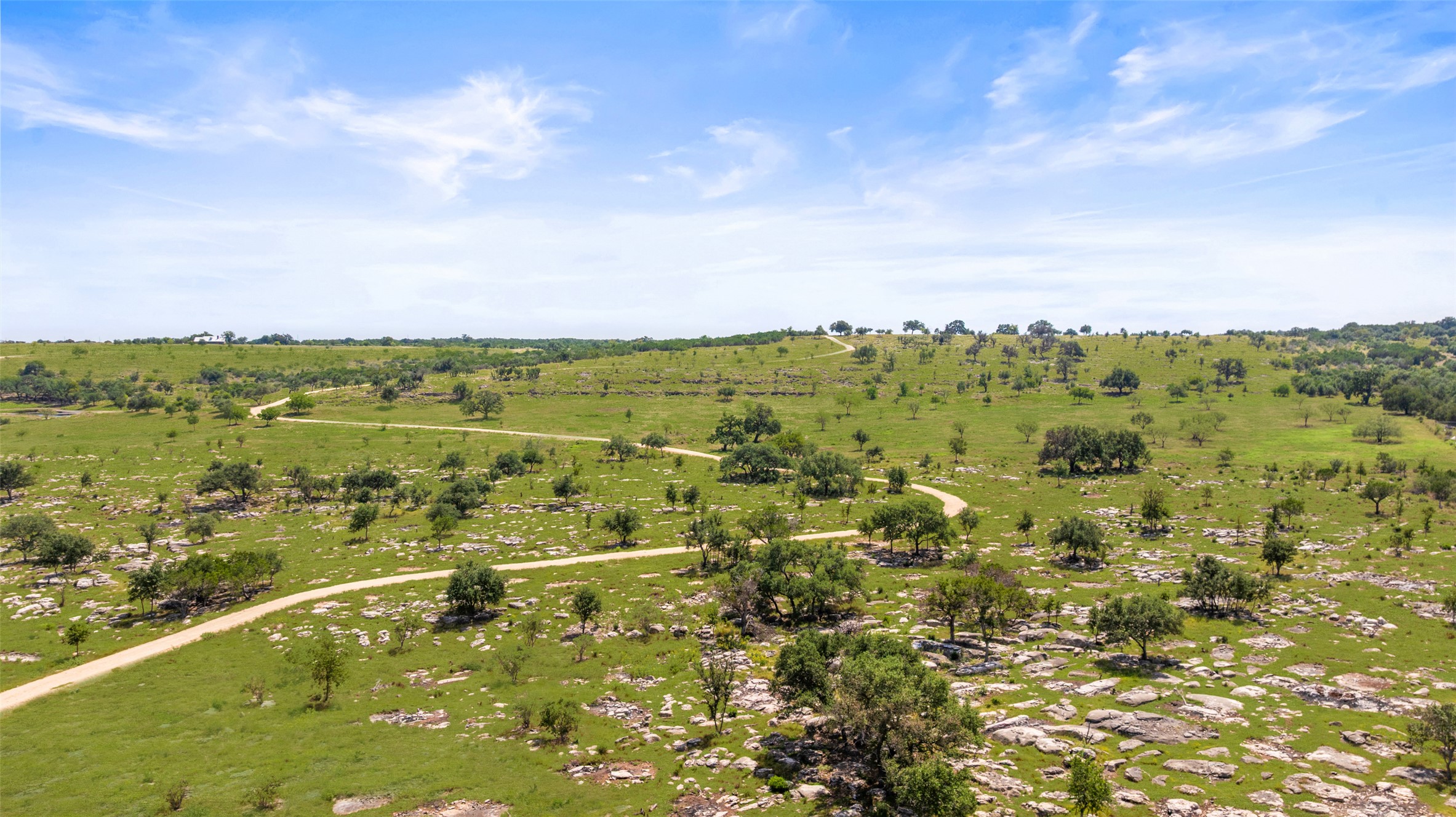 960 Gibson Road Johnson City, TX 78636 - Photo 15 of 19 Rolling green landscape with scattered trees and a winding pathway under an open sky.