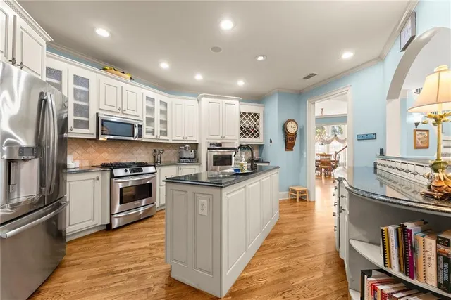 a kitchen with stainless steel appliances granite countertop a stove top oven a sink dishwasher a refrigerator and a dining table with wooden floor