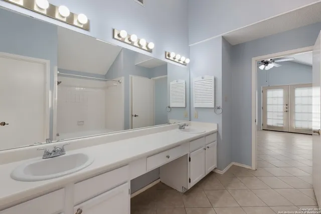 a bathroom with a granite countertop double vanity sink a mirror and a shower