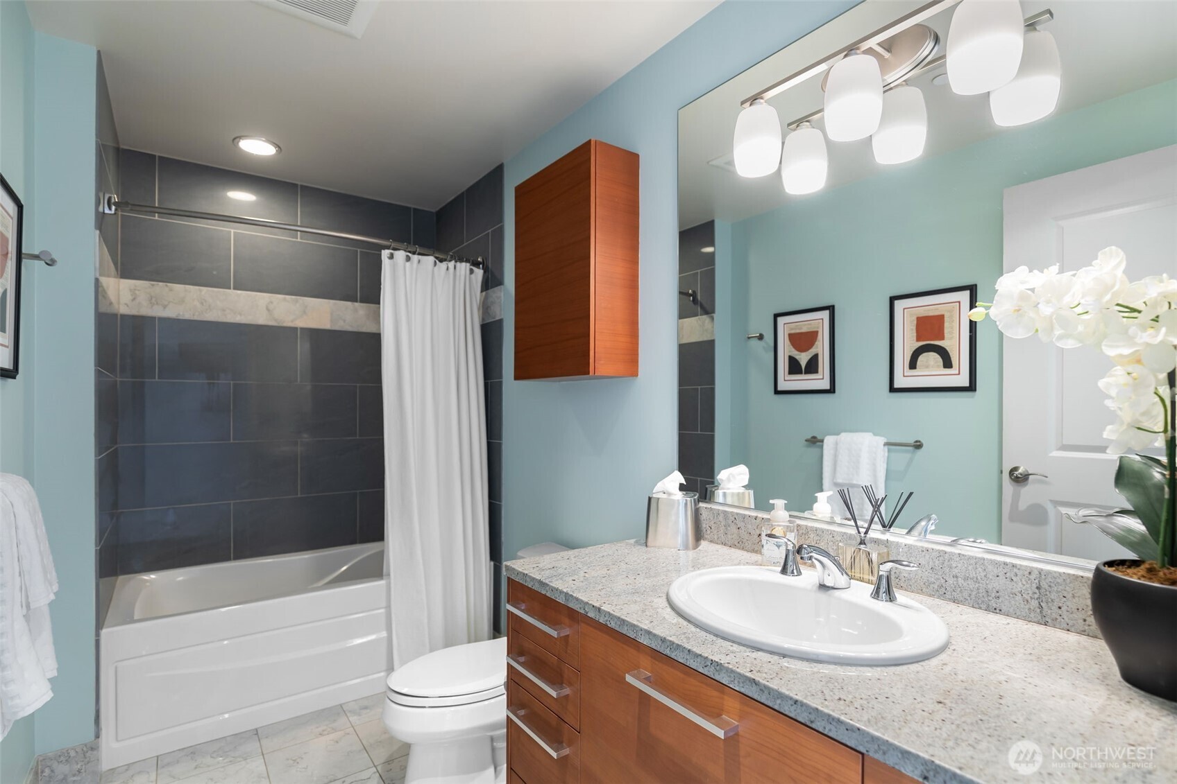 1920 4th Avenue, Unit 1405 Seattle, WA 98101 - Photo 26 of 40 a bathroom with a granite countertop sink a toilet a mirror a vanity a bathtub and shower