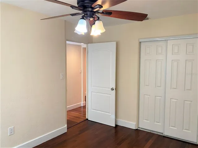 an empty room with wooden floor closet fan and windows