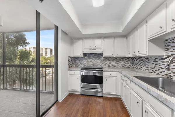 a kitchen with stainless steel appliances granite countertop a stove a sink and white cabinets with wooden floor
