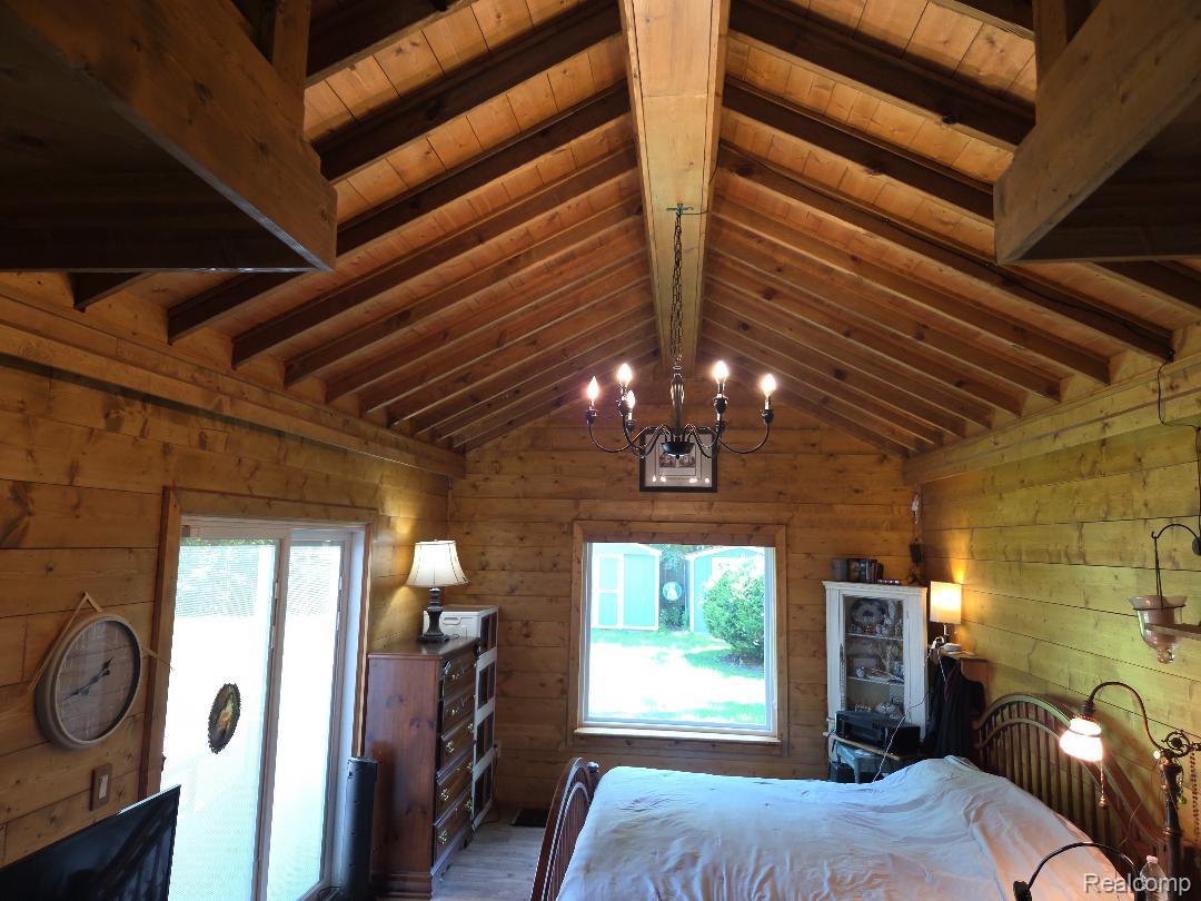 445 Clark Road Highland, MI 48357 - Photo 5 of 7 Vaulted wood-paneled ceiling with exposed beams, illuminated by a central chandelier