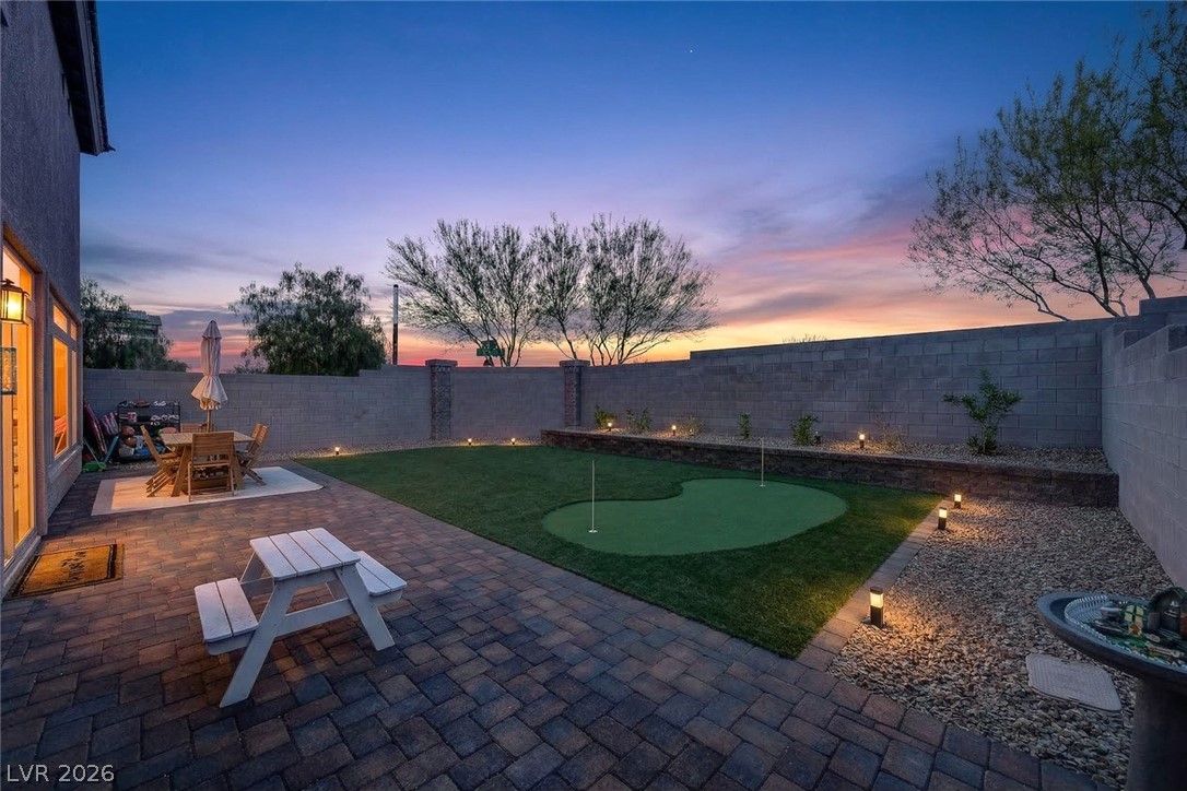 10446 Emerald Rye Street Las Vegas, NV 89183 - Photo 30 of 37 An inviting backyard oasis features a paved patio and a vibrant putting green, perfect for evening relaxation.