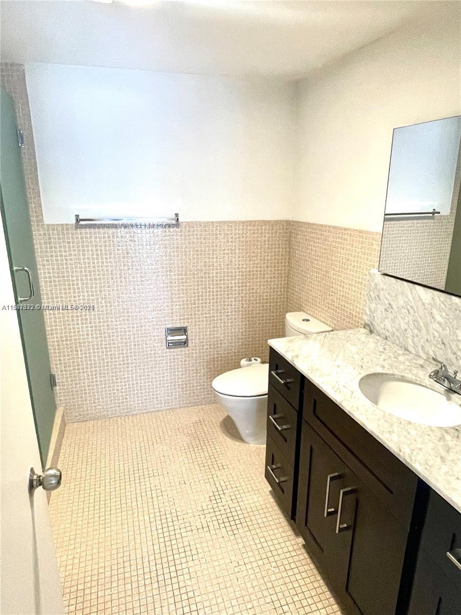 5255 Collins Avenue, Unit 7B Miami Beach, FL 33140 - Photo 10 of 12 a bathroom with a granite countertop sink a toilet a mirror and shower