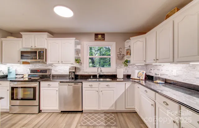 a kitchen with stainless steel appliances granite countertop a stove top oven a sink a dining table and chairs