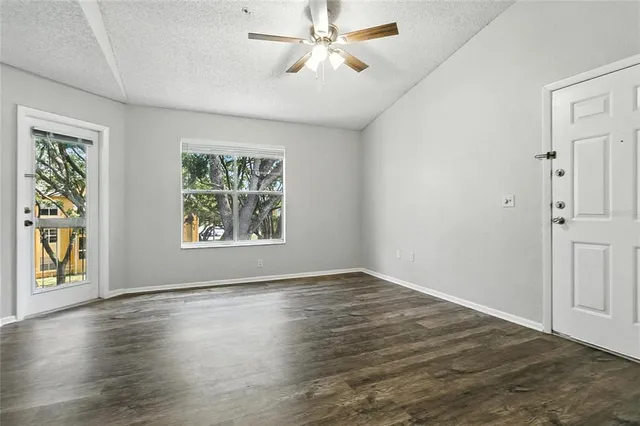 an empty room with wooden floor chandelier fan and windows