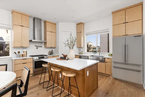 a kitchen with stainless steel appliances granite countertop a stove a refrigerator a sink a dining table and chairs with wooden floor