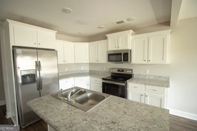 a kitchen with granite countertop a sink stainless steel appliances and white cabinets