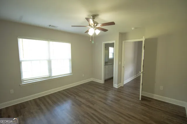 an empty room with wooden floor fan and windows