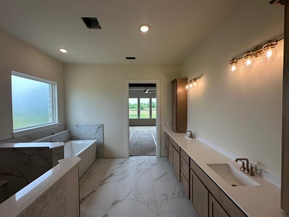205 Cobb Road Leonard, TX 75452 - Photo 19 of 28 Spacious bathroom featuring a built-in soaking tub with a surrounding marbled-finish surround, dual vanities with integrated sinks, and polished chrome fixtures
