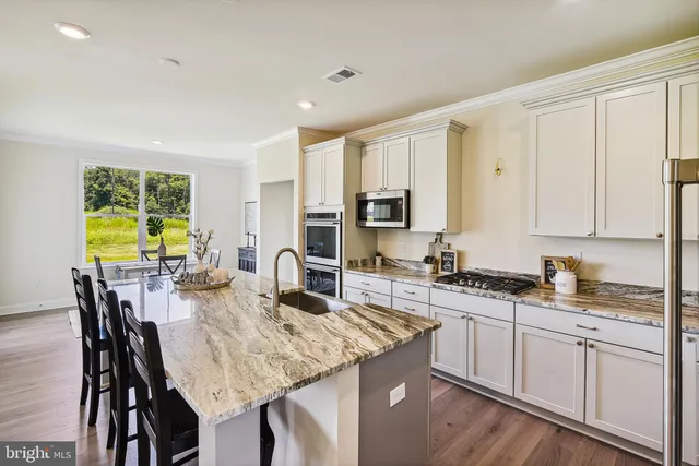 a kitchen with stainless steel appliances granite countertop a stove top oven a sink a refrigerator with white cabinets and wooden floor