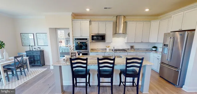 a kitchen with stainless steel appliances granite countertop a dining table chairs refrigerator and microwave