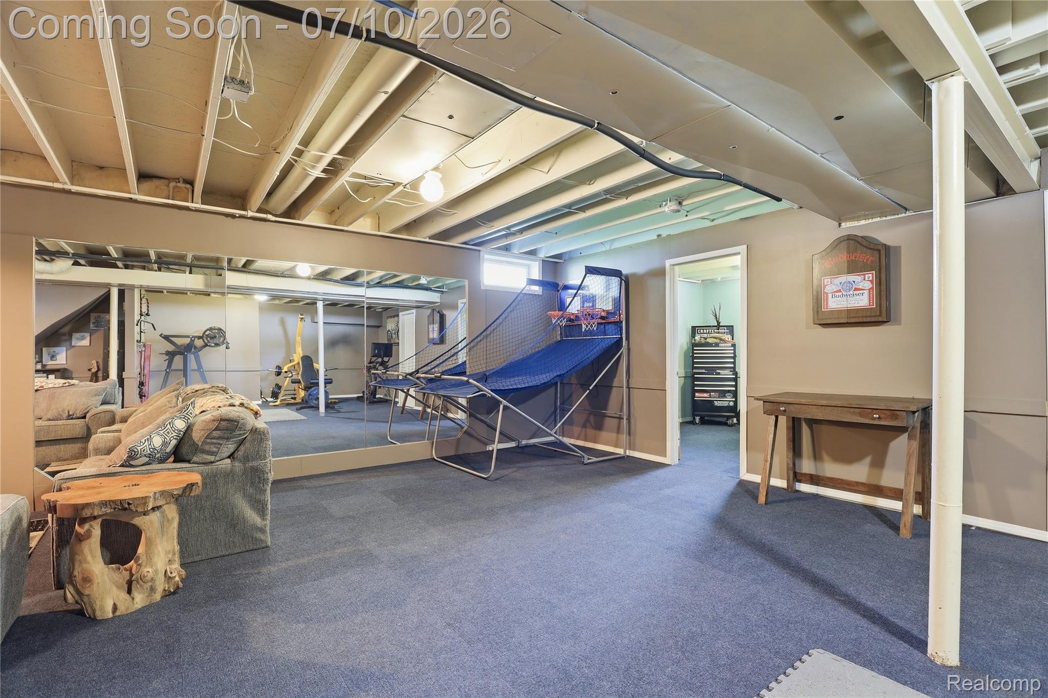 5275 East Maple Avenue Grand Blanc, MI 48439 - Photo 37 of 53 Expansive finished lower level featuring blue carpet flooring, a mirrored wall, exposed ceiling joists, and a doorway opening to an additional area