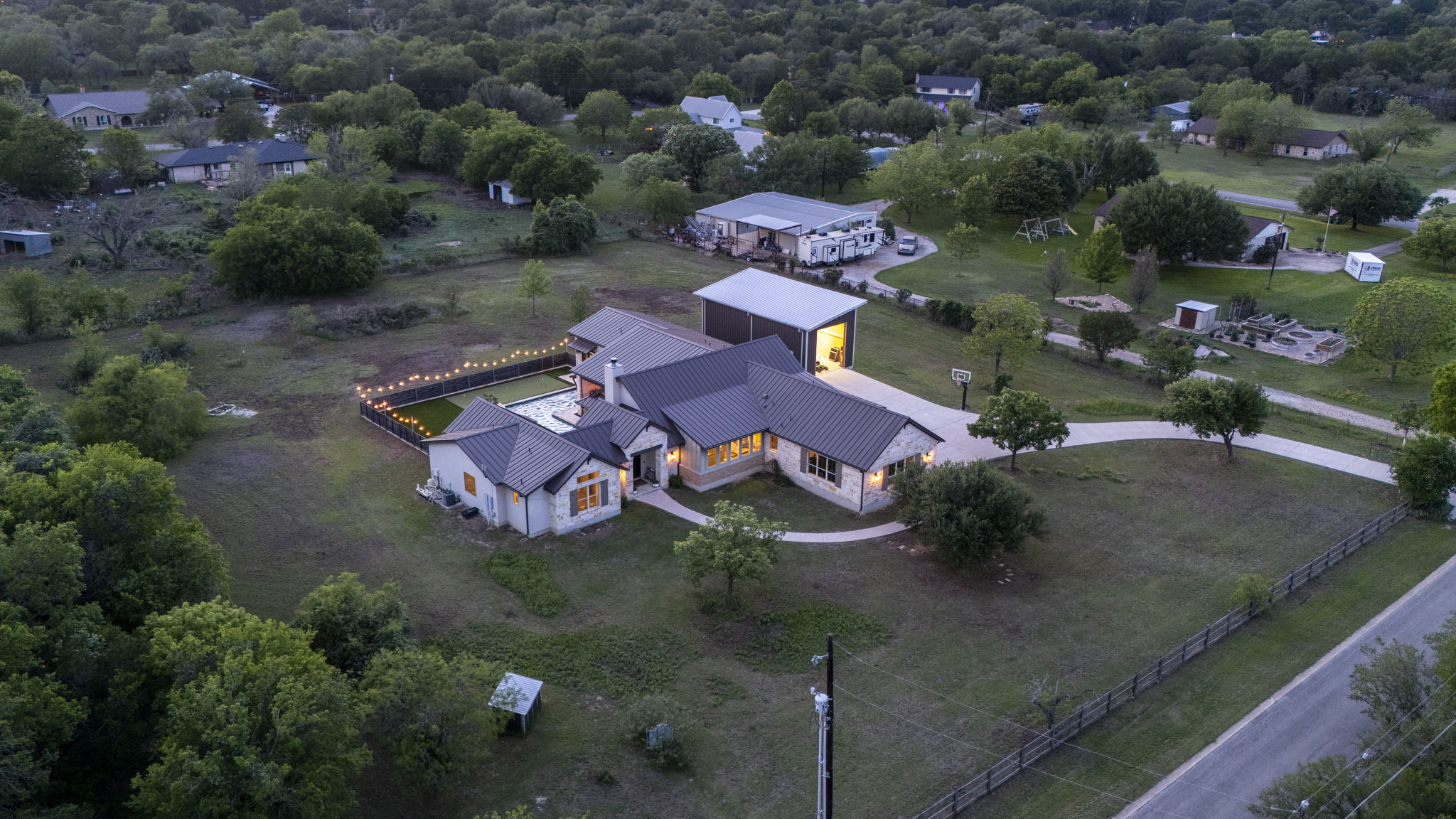 16202 Remuda Trail Buda, TX 78610 - Photo 36 of 40 An aerial view of the property showcasing a single-story residence with a dark roof and light-colored siding, a detached garage, and a swimming pool area with string lights