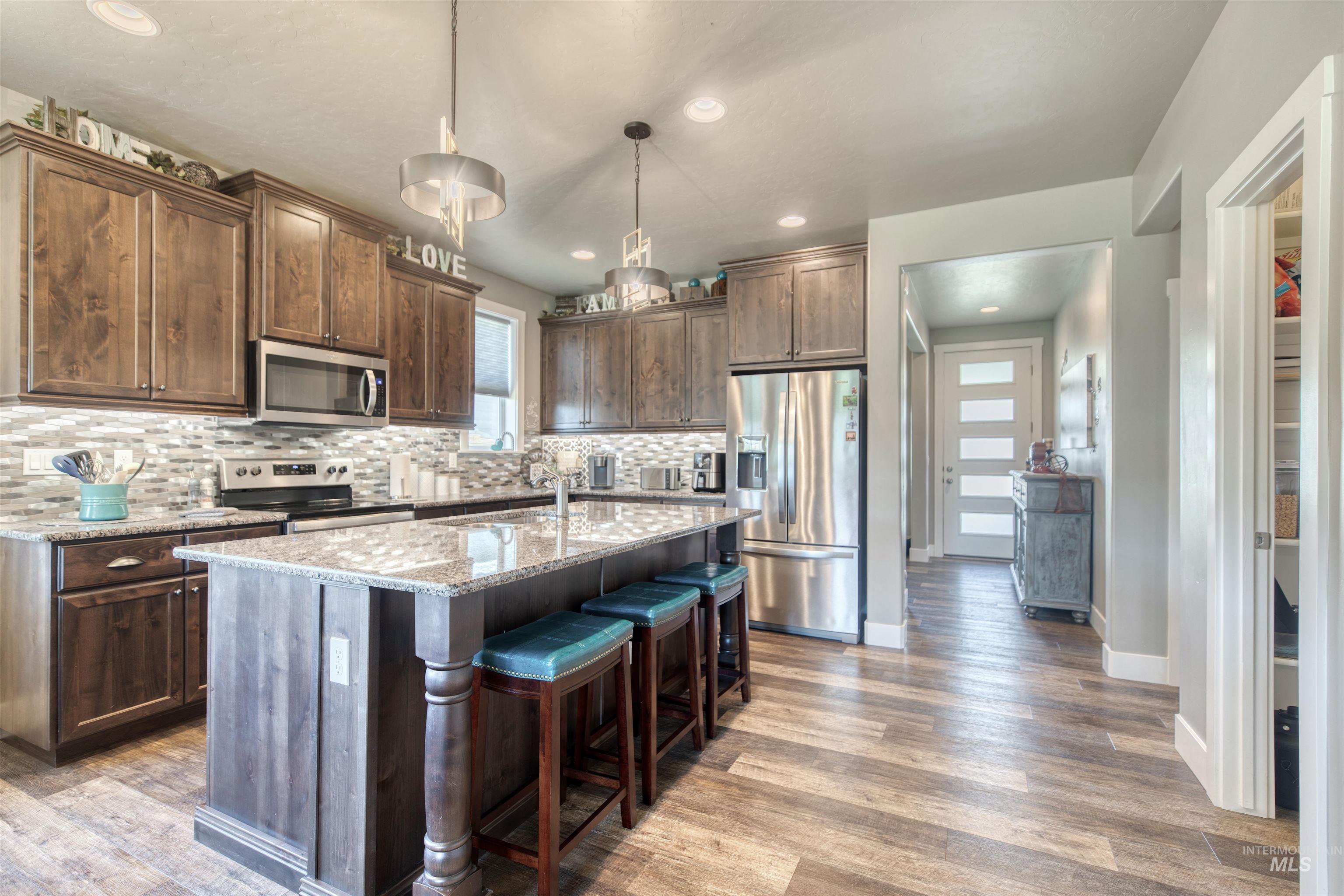 11913 West Piazza Street Nampa, ID 83686 - Photo 7 of 50 Kitchen with light stone counters, appliances with stainless steel finishes, dark brown cabinetry, a kitchen bar, and pendant lighting