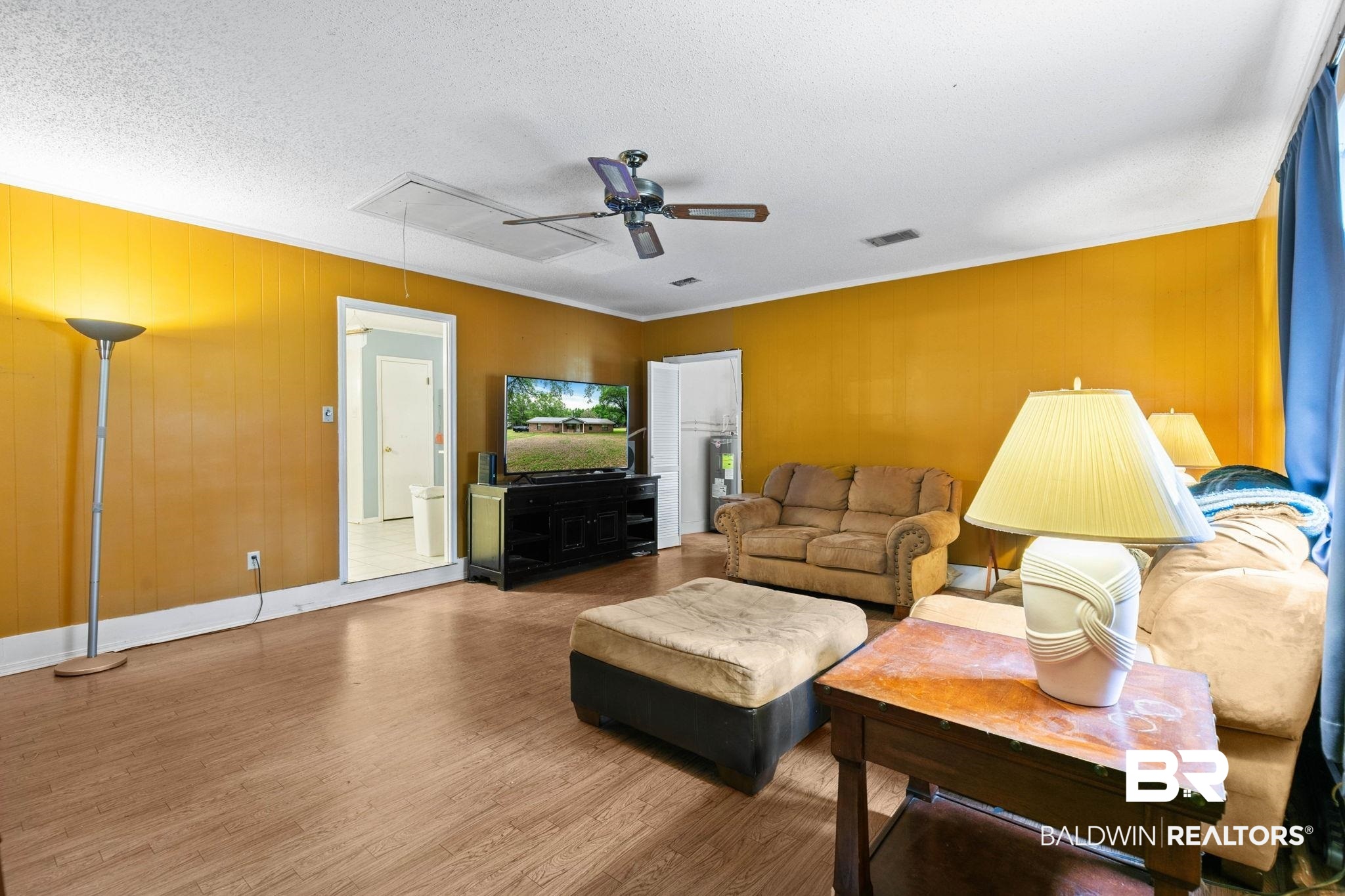 13653 Roberts Road Loxley, AL 36551 - Photo 16 of 33 Spacious living area featuring wood-finish flooring, a white ceiling with a ceiling fan, and vibrant wall paneling