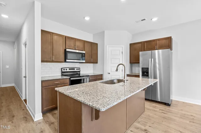 a kitchen with stainless steel appliances granite countertop a refrigerator a stove and a sink with wooden floor