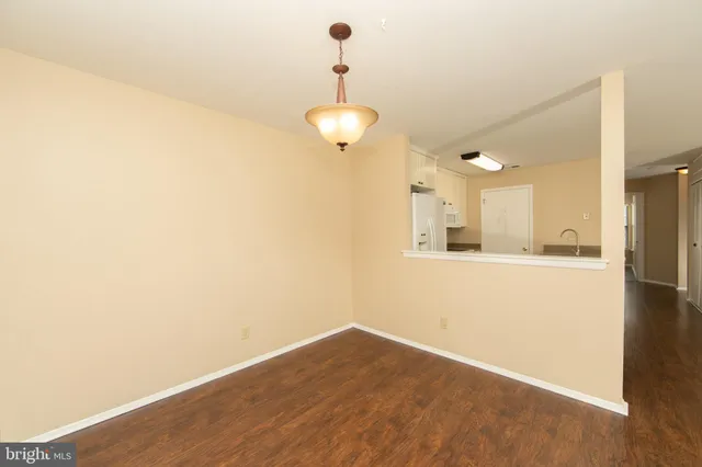 a view of an empty room with wooden floor and a kitchen