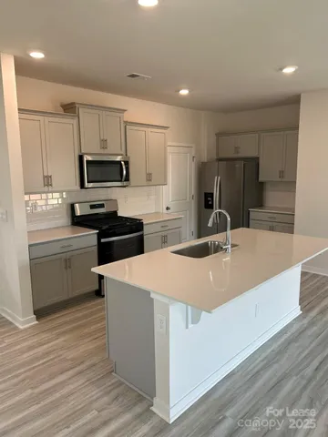 a kitchen with stainless steel appliances a sink dishwasher a stove top oven a refrigerator with white cabinets and wooden floor