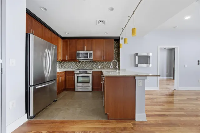 a kitchen with stainless steel appliances granite countertop a refrigerator a stove top oven and a sink with wooden floor