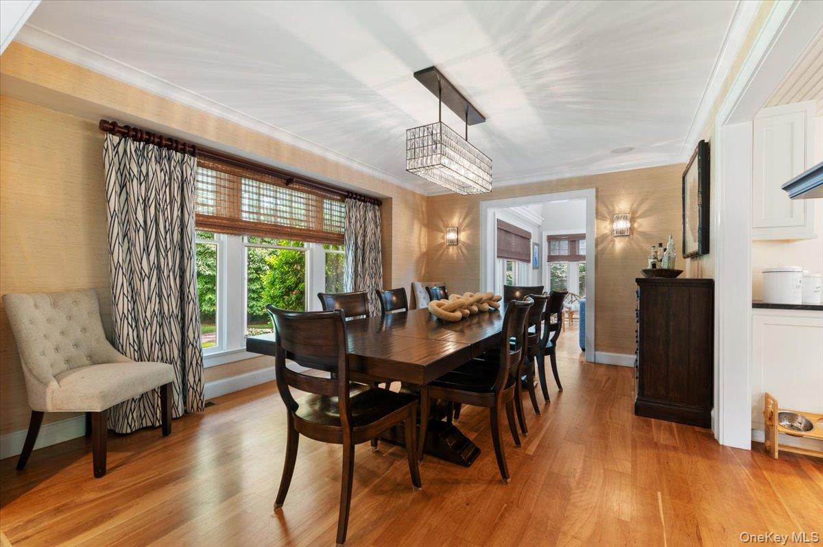 5 Fox Hunt Court Cold Spring Harbor, NY 11724 - Photo 10 of 42 Dining area featuring wood-finish flooring, a large window with exterior landscaping, wall sconces, a contemporary chandelier, and an open doorway