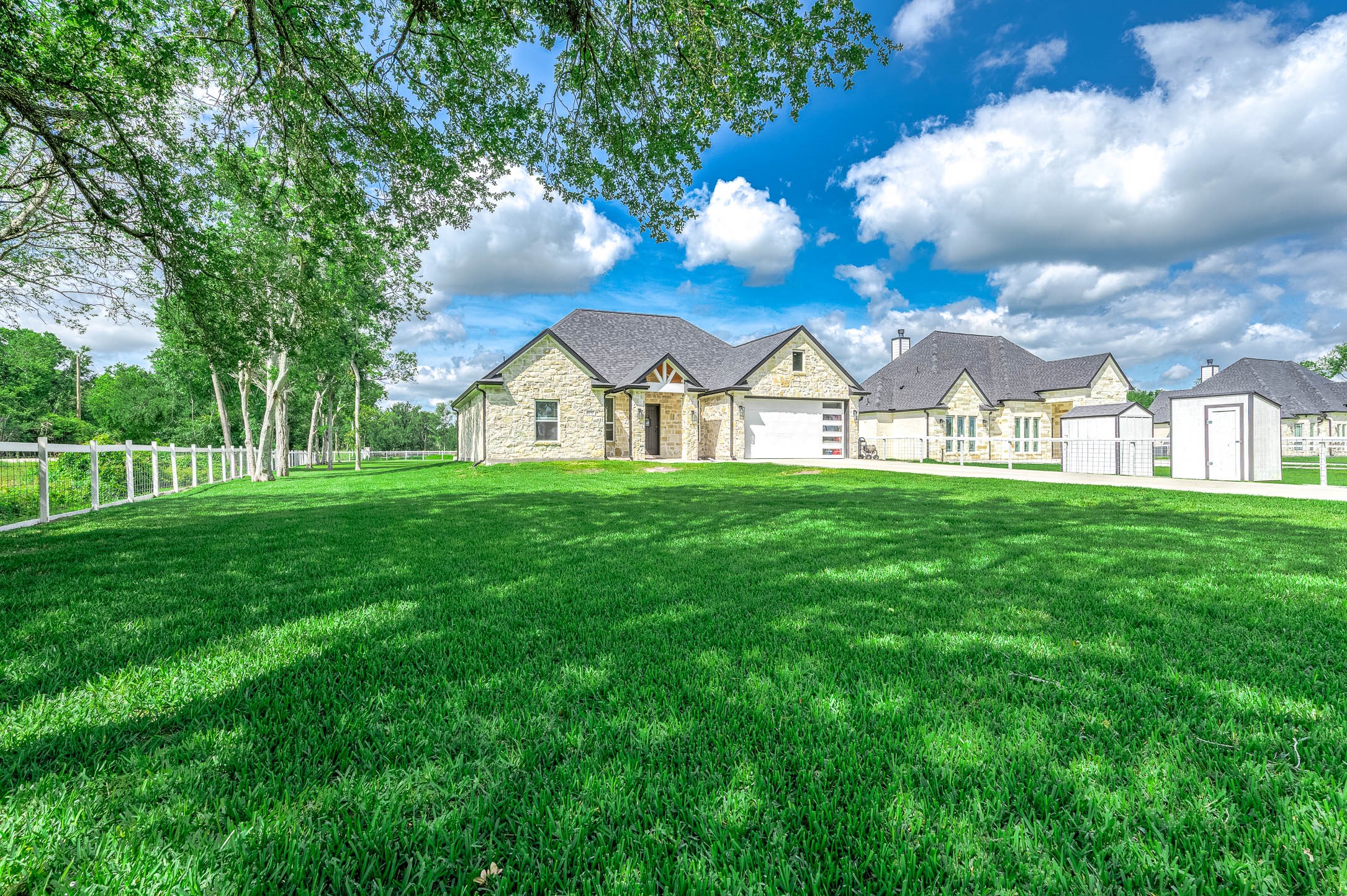 8032 Short Road Needville, TX 77461 - Photo 50 of 50 This spacious stone home is set against a backdrop of mature trees and features a beautifully maintained lawn with fenced outdoor space. The combination of modern design and natural surroundings creates a peaceful and inviting setting.