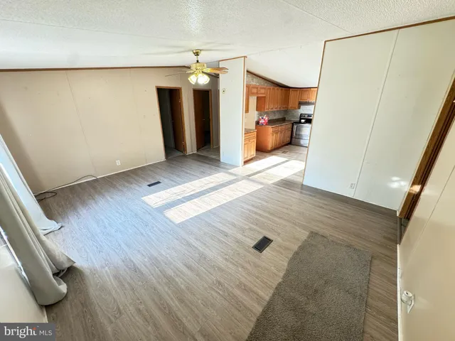 a view of a refrigerator in kitchen and an empty room with wooden floor