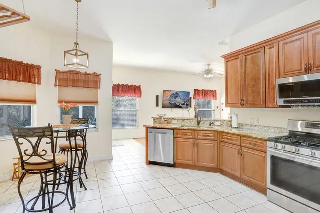 a kitchen with stainless steel appliances granite countertop a stove top oven a sink dishwasher and a refrigerator with wooden cabinets