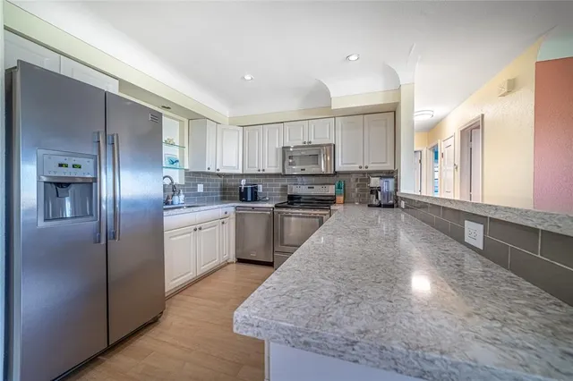 a kitchen with stainless steel appliances granite countertop a refrigerator a sink dishwasher a stove and white cabinets with wooden floor