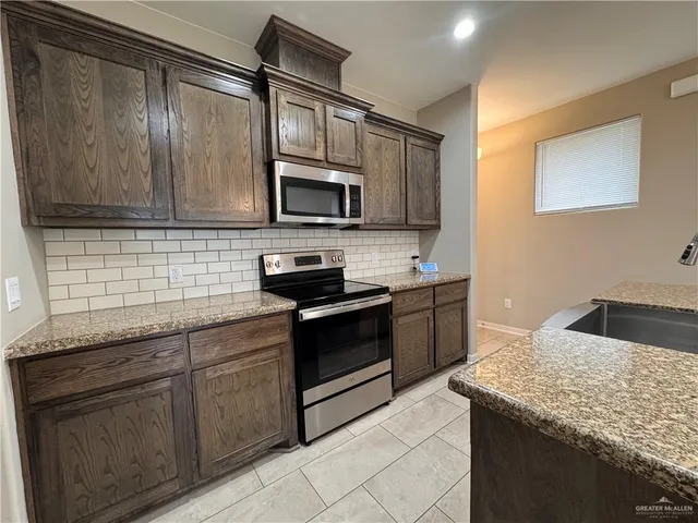 a kitchen with stainless steel appliances granite countertop a sink dishwasher a stove and a microwave oven with cabinets