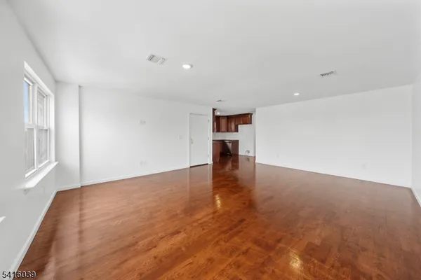 a view of empty room with wooden floor and kitchen
